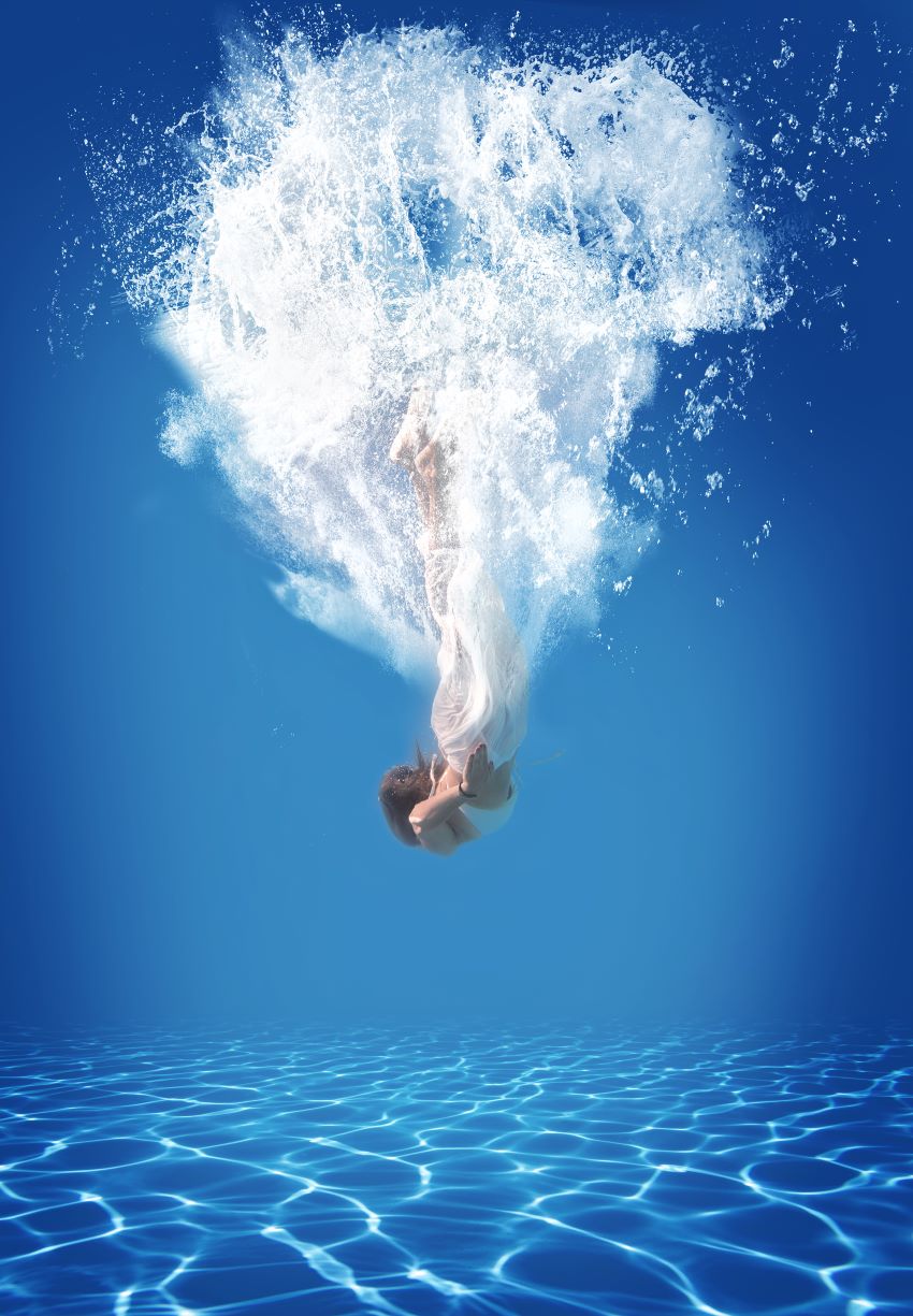 Frau taucht im Schwimmbad ins Wasser, viele Luftblasen.